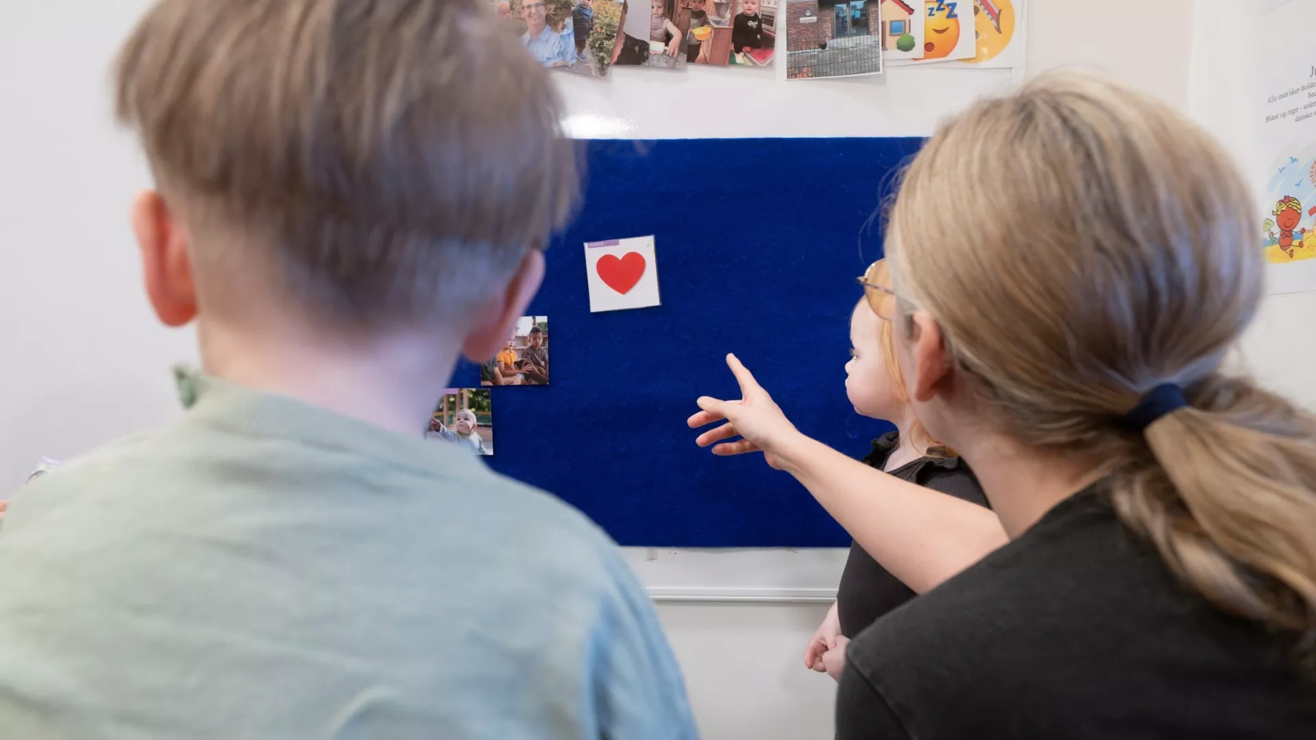 Billedet viser en pædagog pege på billeder sammen med to børn