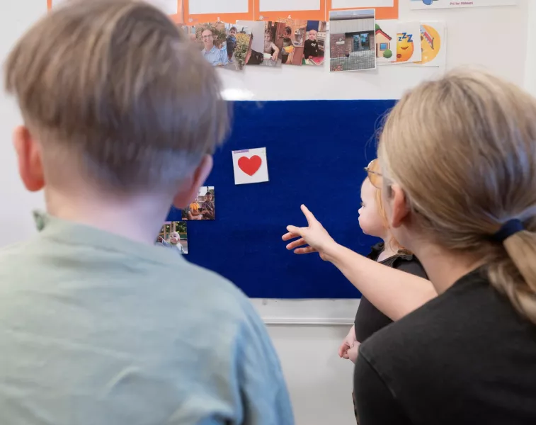 Billedet viser en pædagog pege på billeder sammen med to børn