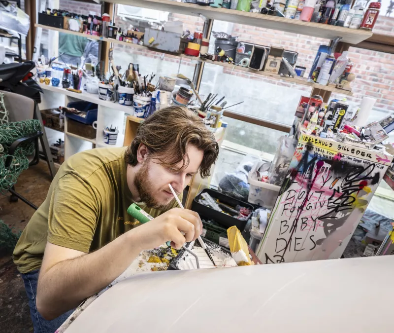 Billedet vider en ung, der maler på en stol som en del af et kunstforløb i Kulturmøllen.